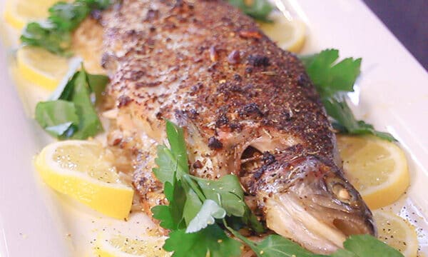baked trout on a white plate, with lemon and parsley alongside it