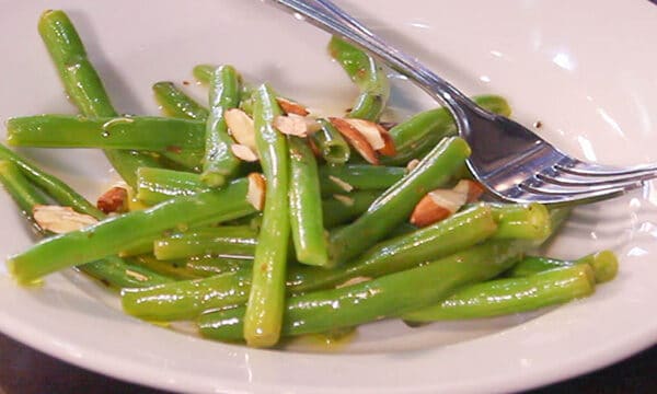 green beans on a white plate with almonds sprinkled on top and a fork along side it