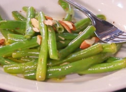 cooked green beans on a plate. They are shiny from being covered in butter. A fork can be seen beside the beans