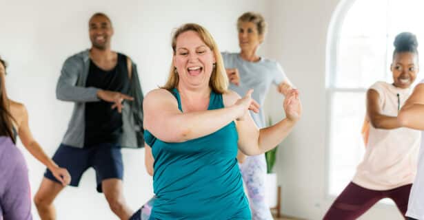 A group of people dance in a room. Each of them wear work out clothes.
