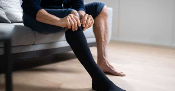 A person sits on a couch and pulls up black compression socks.